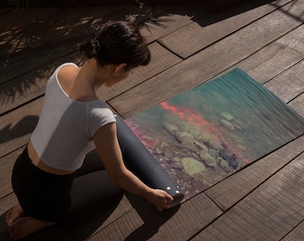 May include: A person rolls up a yoga mat with a colorful underwater scene printed on it. The mat is on a wooden surface.