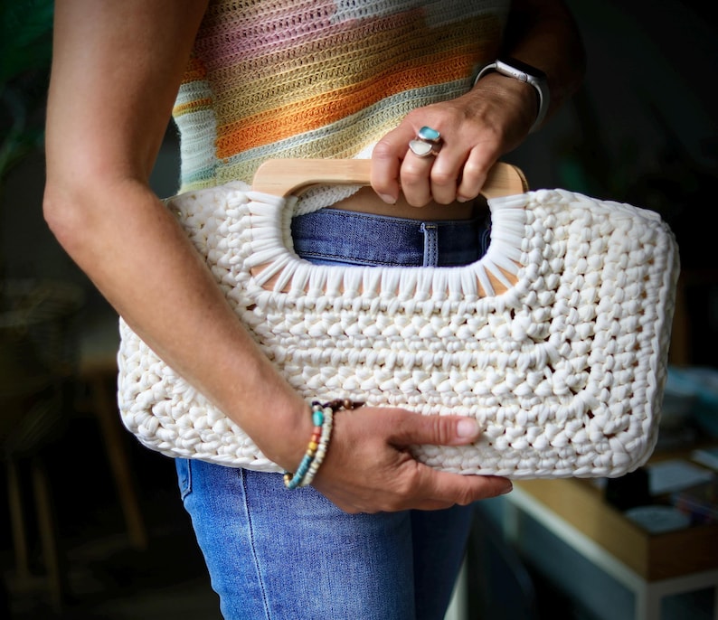Crochet clutch bag pattern with a woman holding the finished bag, made with tshirt yarn and has wooden handles.