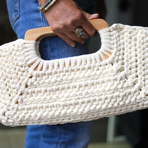 Crochet clutch bag pattern with a woman holding the finished bag, made with tshirt yarn and has wooden handles.