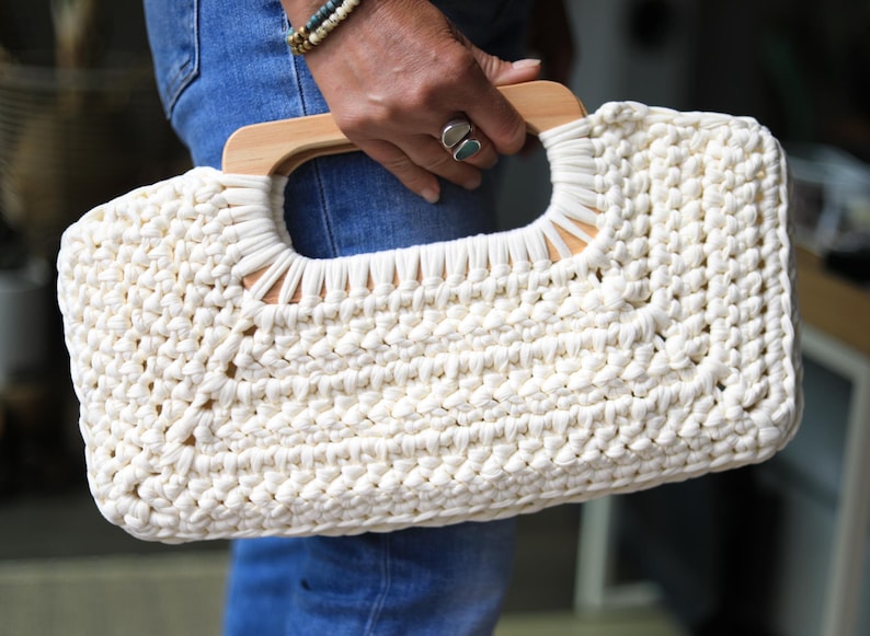 Crochet clutch bag pattern with a woman holding the finished bag, made with tshirt yarn and has wooden handles.