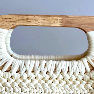 Crochet clutch bag pattern with a woman holding the finished bag, made with tshirt yarn and has wooden handles.