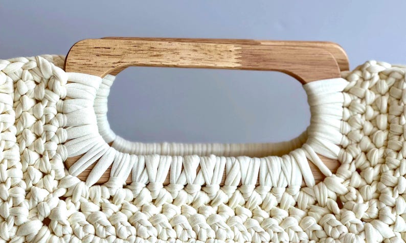 Crochet clutch bag pattern with a woman holding the finished bag, made with tshirt yarn and has wooden handles.