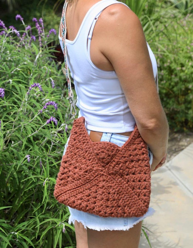 a woman wearing a crossbody granny square bag IN A GARDEN WITH FLOWERS ON A SUNNY DAY