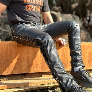 May include: Black leather pants with a lace-up detail on the side. The pants are worn by a person wearing a black t-shirt that says "This is my Halloween costume".