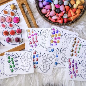 Op de afbeelding: Een set van zes vlinder-vormige leerkaarten met verschillende gekleurde vormen en patronen. De kaarten zijn ontworpen voor kinderen om kleuren, vormen en patronen te leren. De kaarten zijn gemaakt van wit karton en hebben een zwarte omtrek.