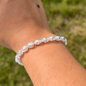 Peut inclure: Un bracelet en argent avec un design délicat et complexe. Le bracelet est composé de petits maillons ronds qui sont reliés entre eux pour former une chaîne. La chaîne mesure environ 18 cm de long et se ferme à l'aide d'un fermoir.