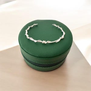 Könnte beinhalten: Ein silbernes Stacheldraht-Armband liegt in einer dunkelgrünen Samt-Ringbox.
