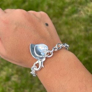 May include: A silver chain bracelet with a heart-shaped charm. The charm has a small inscription on the back.
