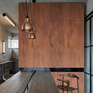 Könnte beinhalten: Innenaufnahme einer modernen Küche mit Holzschrank und Arbeitsplatte. Kupferfarbene Pendelleuchten hängen über der Arbeitsplatte. Der Holzschrank hat eine warme braune Farbe. Zwei Holzstühle sind zu sehen.