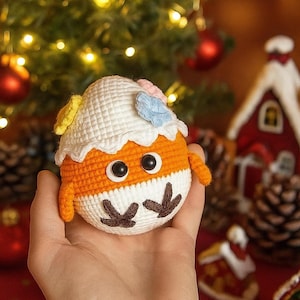 Puede incluir: Adorno hecho a mano en forma de huevo tejido a ganchillo, con cuerpo naranja, base blanca y parte superior blanca con detalles florales coloridos. El adorno tiene ojos negros y pies marrones. Ideal para decoraciones navideñas.
