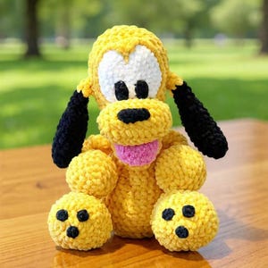 May include: A handmade yellow plush dog with black ears and spots, white eyes, and a pink tongue. The stuffed animal is sitting on a wooden surface, with a blurred green background.