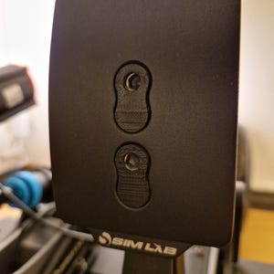 Könnte beinhalten: Eine schwarze Plastikplatte mit zwei runden Löchern und dem Text "SIM LAB" unten aufgedruckt.