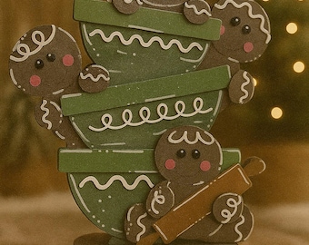 May include: A whimsical Christmas decoration featuring a stack of green mixing bowls with gingerbread men. One gingerbread man wears a Santa hat, another holds a whisk, and another holds a rolling pin. The base is a wooden platform.