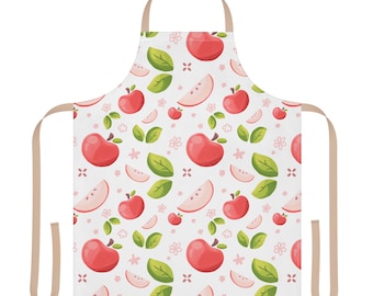 May include: A white apron featuring a repeating pattern of red whole apples, sliced apple segments, green leaves, and small pink flowers. The apron includes light tan neck and waist ties for securing the garment during use.