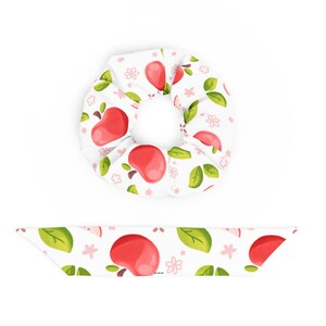 May include: A white fabric hair scrunchie and a matching long fabric hair ribbon, both featuring a repeating pattern of red apples, green leaves, and small pink flowers. The accessories are made of a soft, gathered material.