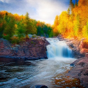 Könnte beinhalten: Ein Wasserfall stürzt über Felsen in einer Waldlandschaft. Die Bäume sind in leuchtenden Herbstfarben, mit Schattierungen von Gelb, Orange und Rot. Das Wasser ist klar und fließt, was ein Gefühl von Frieden und Ruhe vermittelt.