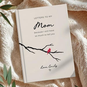 May include: A cream-colored journal titled "Letters to My Mom" with black script and a branch design with a red bird. The journal includes the text "because I still have so much to tell you" and "Love, Emily".