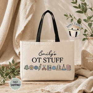 May include: A cream-colored canvas tote bag with black handles and an inner zipper. The front features the black text "Emily's OT STUFF" above a row of colorful icons including a puzzle piece, flower, button, pencil, scissors, and various therapy tools.