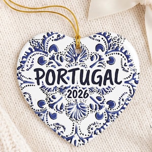 May include: A heart-shaped ceramic ornament featuring a blue and white tile-inspired pattern. The text PORTUGAL is printed in dark blue across the center, with the year 2026 below it. A gold string is attached to the top for hanging purposes.