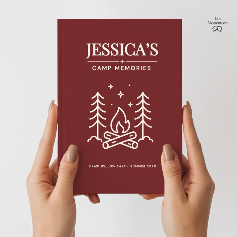 May include: A maroon journal with white text reading "JESSICA'S + CAMP MEMORIES". A white illustration of a campfire with trees and stars is below the title. The bottom of the journal reads "CAMP WILLOW LAKE &bull; SUMMER 2026".
