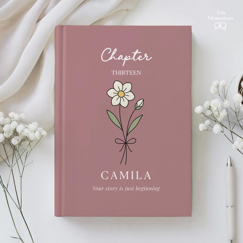 May include: A mauve-colored journal with the word "Chapter" and "THIRTEEN" in white script. A floral illustration is centered below the text. The name "CAMILA" is printed below the illustration, with the phrase "Your story is just beginning."