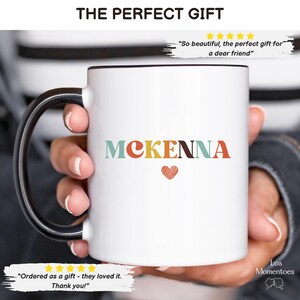 Puede incluir: Taza de cer&aacute;mica blanca con asa negra. La taza tiene el nombre "MCKENNA" impreso en letras de colores con un coraz&oacute;n rojo.
