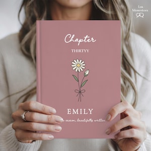 May include: A hardcover journal with a dusty rose cover. The cover features the word "Chapter" in script, the number "THIRTYY", a daisy illustration, and the name "EMILY". The journal also has the text "in season, beautifully written".