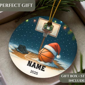 May include: Round Christmas ornament with a basketball theme. The ornament features a basketball wearing a Santa hat, a basketball hoop, and a pair of sneakers. The text "NAME" and "2025" are displayed on the ornament.