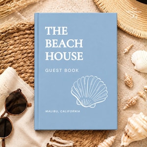 May include: A light blue hardcover guest book with white text that reads THE BEACH HOUSE GUEST BOOK and MALIBU, CALIFORNIA. The cover features a white line drawing of a seashell centered on the lower right side of the book's front cover.