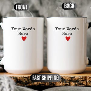 May include: Two white ceramic mugs with black handles and rims. Each mug has the text "Your Words Here" above a red heart. The mugs are displayed on a wooden surface.
