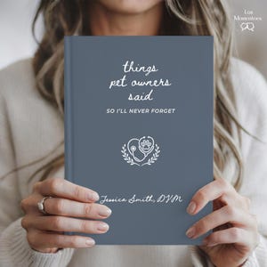 May include: A blue journal with the text "things pet owners said" and "SO I'LL NEVER FORGET". The journal features a paw print and stethoscope design, with the name "Jessica Smith, DVM" at the bottom. The journal is held by a person.