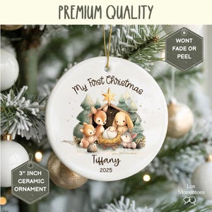 May include: A white ceramic Christmas ornament, 3 inches in diameter, with a watercolor illustration of a nativity scene. The ornament reads "My First Christmas", "Tiffany", and "2025". The ornament is hanging on a Christmas tree.