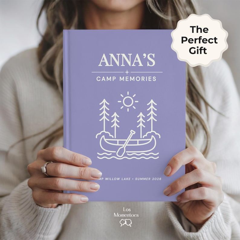 May include: A lilac journal with the text "ANNA'S + CAMP MEMORIES" and a canoe illustration. The text "CAMP WILLOW LAKE - SUMMER 2026" is at the bottom. A white sticker says "The Perfect Gift".