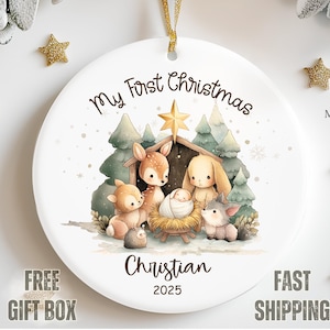 May include: White ceramic Christmas ornament with a watercolor illustration of a nativity scene with woodland animals. The text "My First Christmas" and "Christian 2025" are displayed on the ornament.