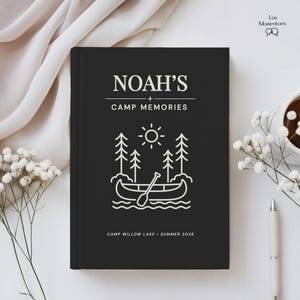 May include: A black journal featuring the text "NOAH'S CAMP MEMORIES" in white. The cover has a line drawing of a canoe, trees, and sun. The journal also includes the text "CAMP WILLOW LAKE - SUMMER 2026".