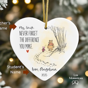 May include: A heart-shaped white ceramic ornament featuring a gold hanging ribbon. It displays a Winnie the Pooh and Piglet illustration with the text: Mrs. Smith, NEVER FORGET THE DIFFERENCE YOU MAKE, Love, Angelina, and the year 2025.