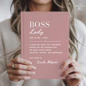 May include: A dusty rose hardcover book with white text that reads BOSS Lady, followed by a phonetic pronunciation, the definition of a woman who leads with confidence, and the custom name Camila Delgado printed at the bottom of the cover.