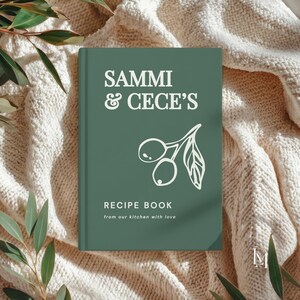 May include: A dark green hardcover recipe book with white text that reads SAMMI & CECE'S, RECIPE BOOK, and from our kitchen with love. The cover features a white line drawing of two olives on a branch with a single leaf centered on the front.
