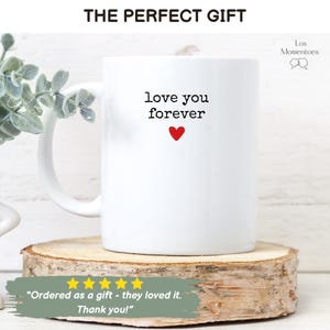 May include: White ceramic mug with the words "love you forever" and a red heart. The mug is on a wooden slice, with the text "THE PERFECT GIFT" above it. Below the mug is a customer review.