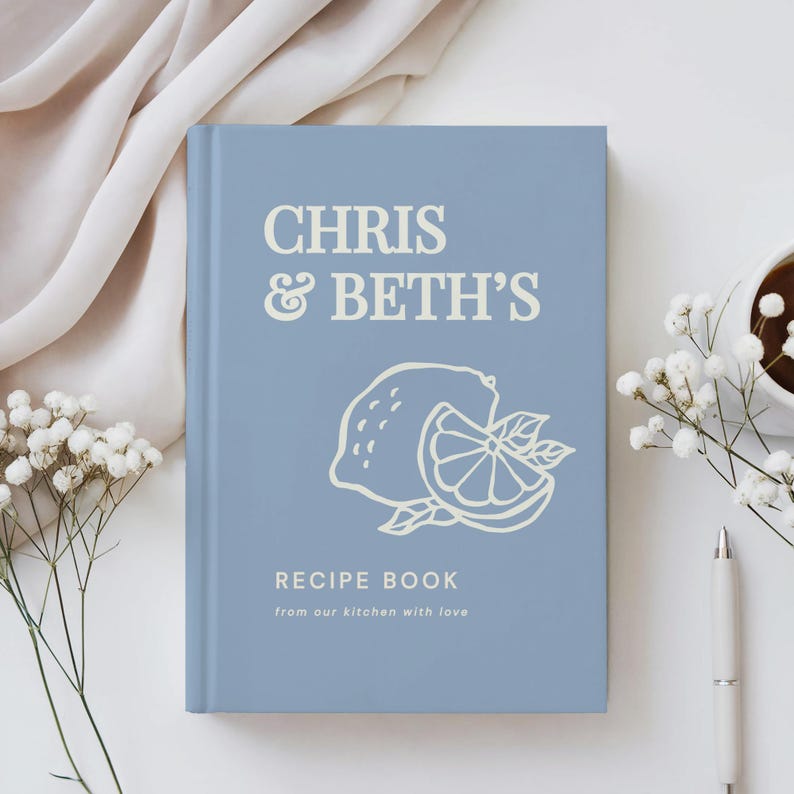 May include: A light blue hardcover recipe book featuring the white text CHRIS & BETH'S RECIPE BOOK from our kitchen with love and a line art illustration of a whole lemon and a sliced lemon half centered on the front cover.