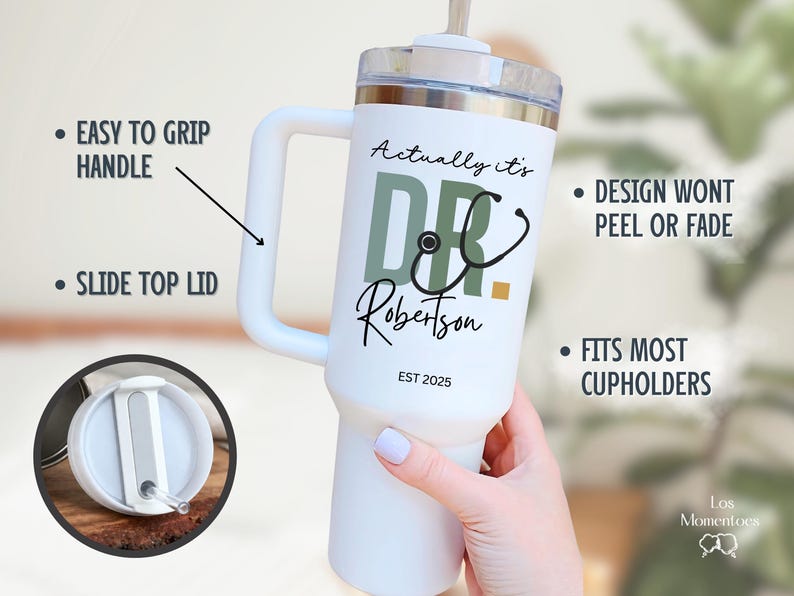 May include: White insulated tumbler with a handle, featuring the text "Actually it's DR Robertson EST 2025" and a stethoscope graphic. The tumbler has a slide top lid and is designed to fit most cupholders.
