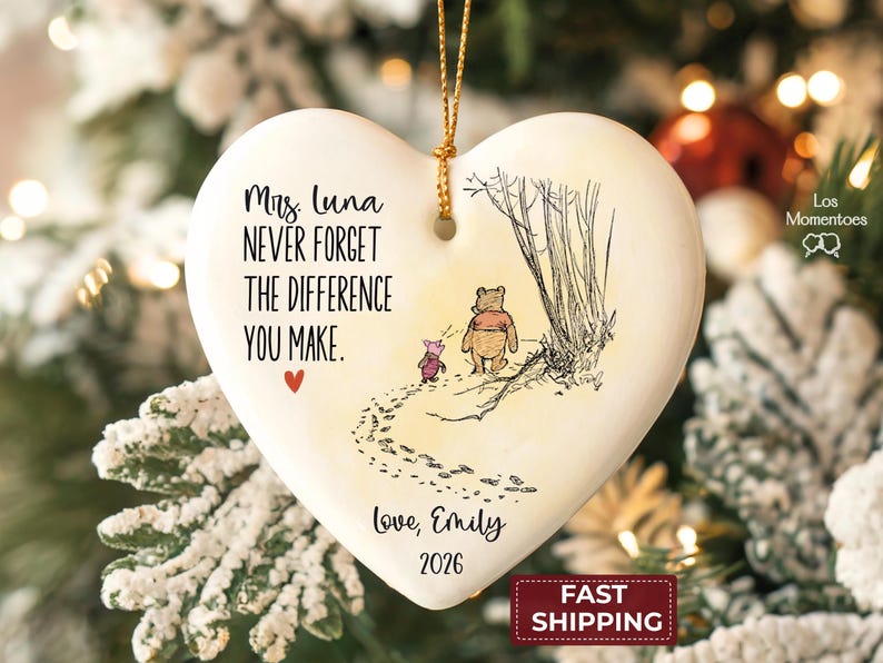 May include: A heart-shaped white ceramic ornament featuring a black ink illustration of Winnie the Pooh and Piglet walking. Text reads: Mrs. Luna NEVER FORGET THE DIFFERENCE YOU MAKE. Love, Emily 2026. A small red heart and gold hanging string.