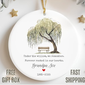 May include: White ceramic ornament with a willow tree illustration, a bench, and text that reads "Under the willow, we remember. Forever rooted in our hearts. Grandpa Joe 1965-2025." Gold star ornaments are scattered around the ornament.