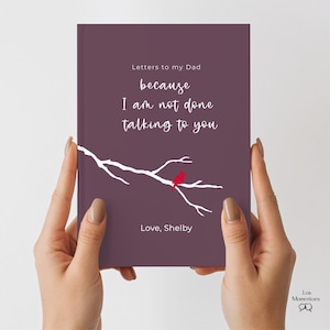 Op de afbeelding: Een paars notitieboek met de titel "Letters to my Dad" met witte tekst en een takontwerp met een rode vogel. De tekst luidt "because I am not done talking to you" en "Love, Shelby".