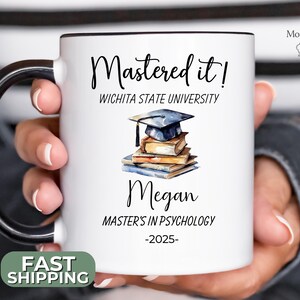 May include: White ceramic mug with a black handle and rim. The mug features the text "Mastered it!" and "Wichita State University". Below is the name "Megan", the text "MASTER'S IN PSYCHOLOGY -2025-", and a watercolor illustration of books and a graduation cap.