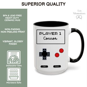 K&ouml;nnte beinhalten: Wei&szlig;er Keramikbecher mit schwarzem Innenraum und Griff. Der Becher hat ein Retro-Videospiel-Controller-Design mit dem Text "PLAYER 1 Connor". Der Becher ist sp&uuml;lmaschinen- und mikrowellengeeignet.