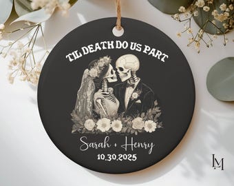 May include: A round black ceramic ornament featuring a white illustration of two skeletons in wedding attire, a veil, and flowers. The text reads TIL DEATH DO US PART, Sarah + Henry, and 10.30.2025. A brown twine loop is attached at the top.