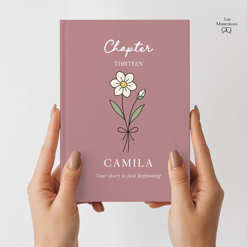 May include: A mauve-colored book cover with the word "Chapter" in white script above "THIRTEEN". A daisy illustration is centered below the text, with the name "CAMILA" and the phrase "Your story is just beginning" below. The book is held by two hands.