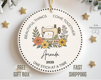 May include: A round, cream-colored ornament with a sewing machine illustration surrounded by flowers. The text reads "BEAUTIFUL THINGS COME TOGETHER" and "ONE STICH AT A TIME". The name "Amanda" and the year "2025" are also displayed.