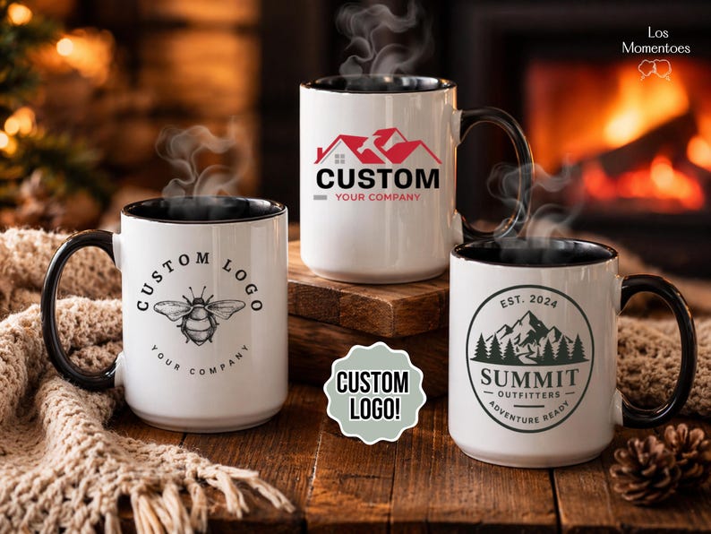May include: Three white ceramic mugs with black handles and rims, each with a custom logo. One has a bee graphic, another a house logo, and the third a mountain and tree design. Steam rises from the mugs, suggesting a hot beverage.